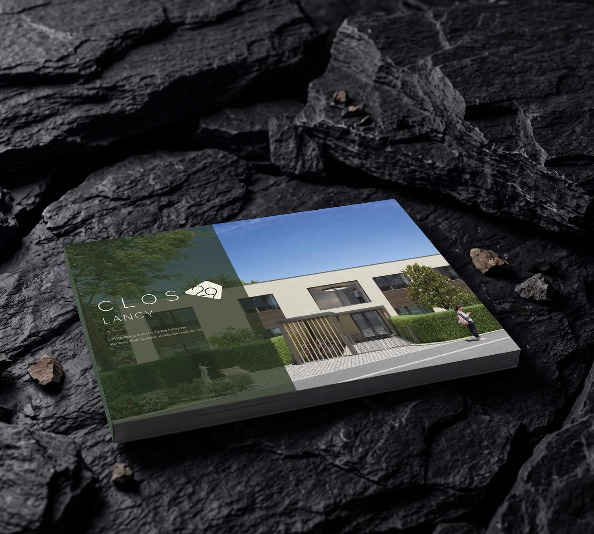 La brochure de vente du Clos 29, couverture vert sombre avec vue 3D des villas, posée sur de l’ardoise